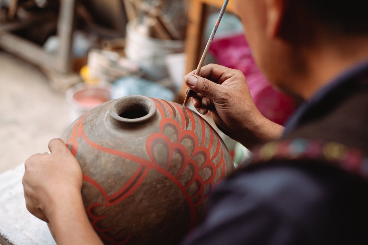 Close-up of an artisan meticulously painting a traditional ceramic pot, showcasing cultural craftsmanship.